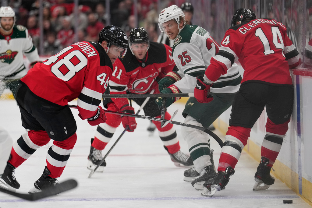 Minnesota Wild's Jonas Brodin (25), second from right, tries to get the puck past New Jersey Devils' Brian Halonen, left, and Luke Glendening, right, during the first period of an NHL hockey game Wednesday, Oct. 22, 2025, in Newark, N.J. (AP Photo/Seth Wenig)