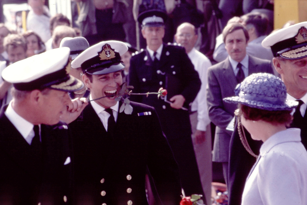 FILE - Britain's Prince Andrew bites the stem of a red rose after stepping ashore from the aircraft carrier HMS Invincible at Portsmouth Harbour, England, on Sept. 17, 1982. Queen Elizabeth II and Prince Philip, right, smile at their sons antics. (AP Photo/David Cauklin, file)