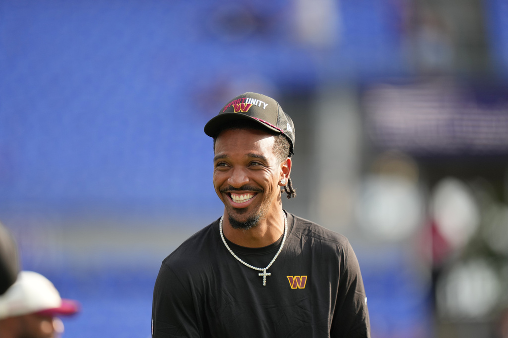 Washington Commanders quarterback Jayden Daniels smiles while watching warmups before an NFL preseason football game against the Baltimore Ravens, Friday, Aug. 28, 2026, in Baltimore. (AP Photo/Stephanie Scarbrough)