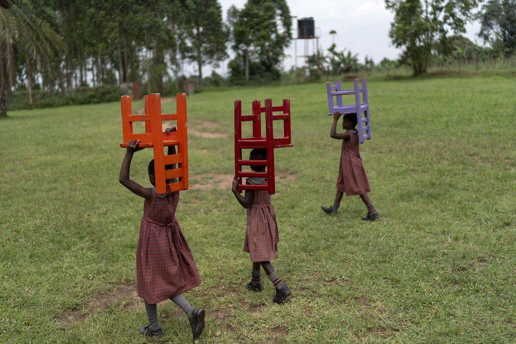 Students carry their chairs at a school for children being raised by their grandparents run by the NGO Reach One Touch One Ministries to help support seniors in the community, in Magogo, Uganda, Saturday, Nov. 16, 2024. (AP Photo/David Goldman)