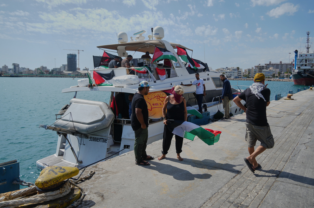 Activists stand in front of one of the Gaza-bound civilian flotilla Sumud's boats as it is docked at the port in Larnaca, Cyprus, on Friday, Oct. 3, 2025. (AP Photo/Petros Karadjias)