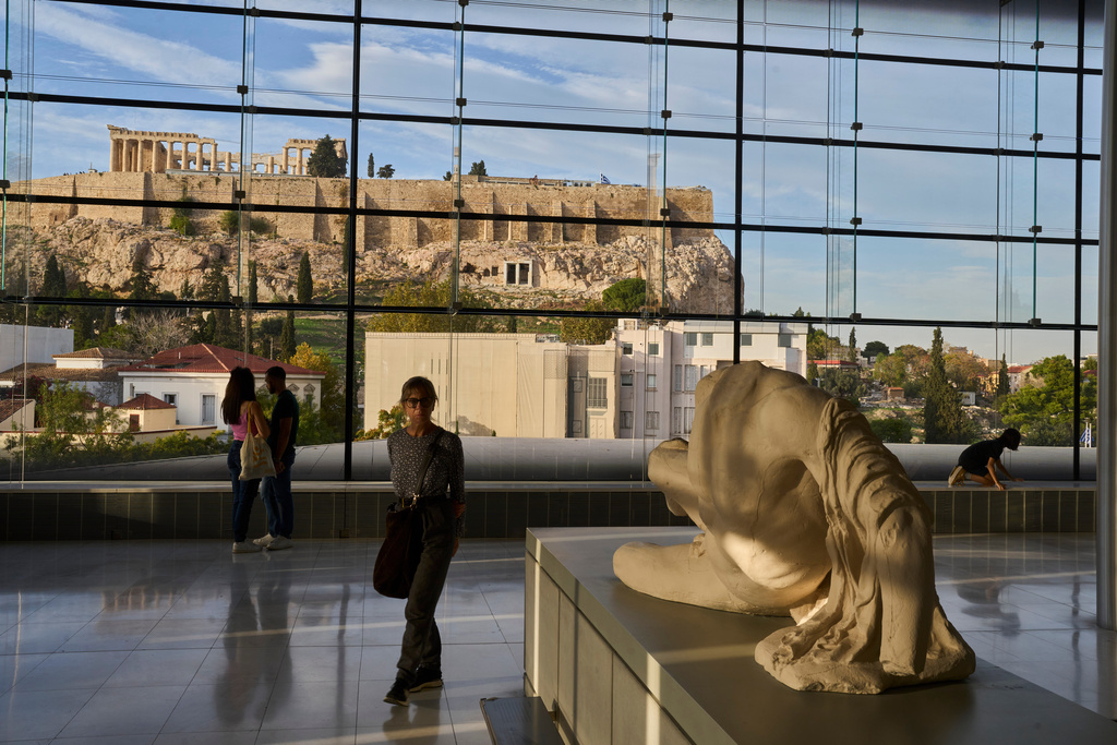 People visit the Acropolis museum as the 5th century B.C. Parthenon temple stands atop the Acropolis hill in the background in Athens, Monday, Oct. 27, 2025. (AP Photo/Petros Giannakouris)