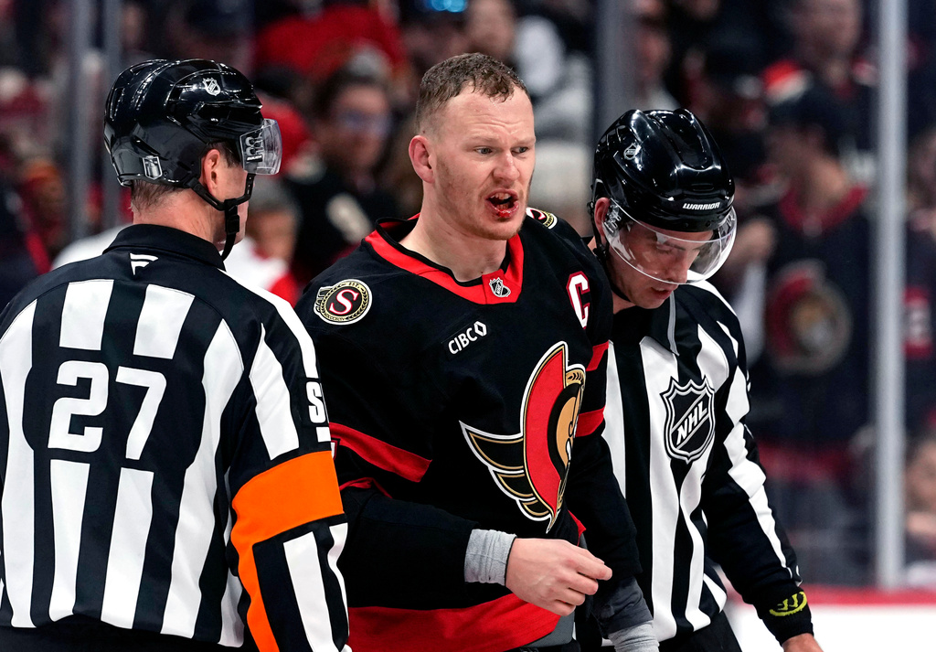 Ottawa Senators winger Brady Tkachuk's lip bleeds as he is escorted by officials after fighting with Carolina Hurricanes' K'andre Miller during the second period in Game 4 of a first-round NHL Stanley Cup playoff hockey series, Saturday, April 25, 2026, in Ottawa, Ontario. (Justin Tang/The Canadian Press via AP)
