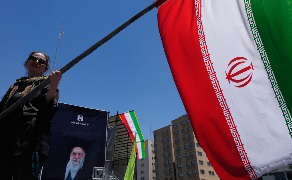 A woman waves an Iranian flag during a pro-government campaign as a portrait of the slain Supreme Leader Ayatollah Ali Khamenei, who was killed in U.S. and Israeli strikes on Feb. 28, is displayed at rear, in downtown Tehran, Iran, Monday, June 15, 2026. (AP Photo/Vahid Salemi)