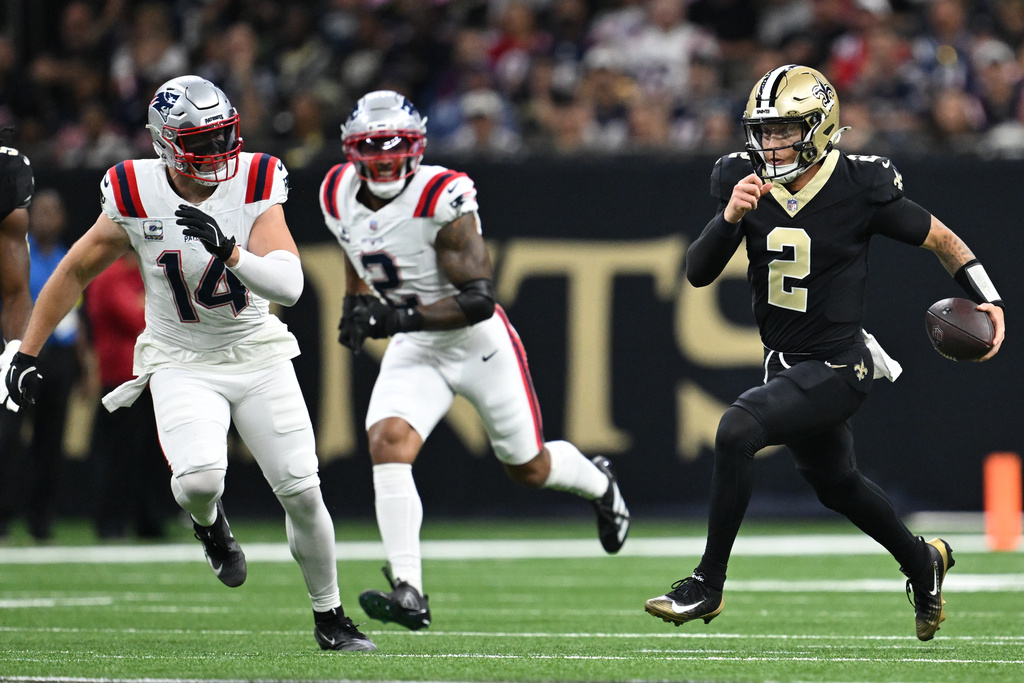 New Orleans Saints quarterback Spencer Rattler, right, runs under pressure from New England Patriots linebackers Robert Spillane, left, and Harold Landry III during the first half of an NFL football game, Sunday, Oct. 12, 2025, in New Orleans. (AP Photo/Ella Hall)