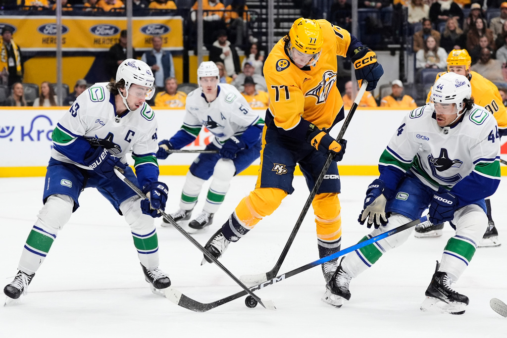 Nashville Predators right wing Luke Evangelista (77) battles Vancouver Canucks defenseman Quinn Hughes (43) and left wing Kiefer Sherwood (44) for the puck during the second period of an NHL hockey game Monday, Nov. 3, 2025, in Nashville, Tenn. (AP Photo/George Walker IV)