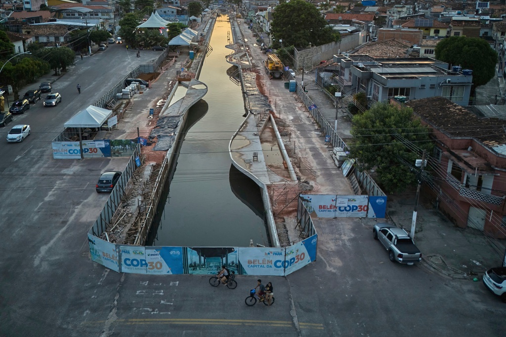 FILE - People ride bikes near signage for the upcoming COP30 U.N. Climate Summit in Belem, Brazil, March 23, 2025. (AP Photo/Jorge Saenz, File)