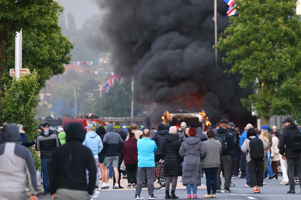 People watch as a vehicle burns during a protest following a stabbing incident in North Belfast, Tuesday, June 9, 2026. (AP Photo/Peter Morrison)