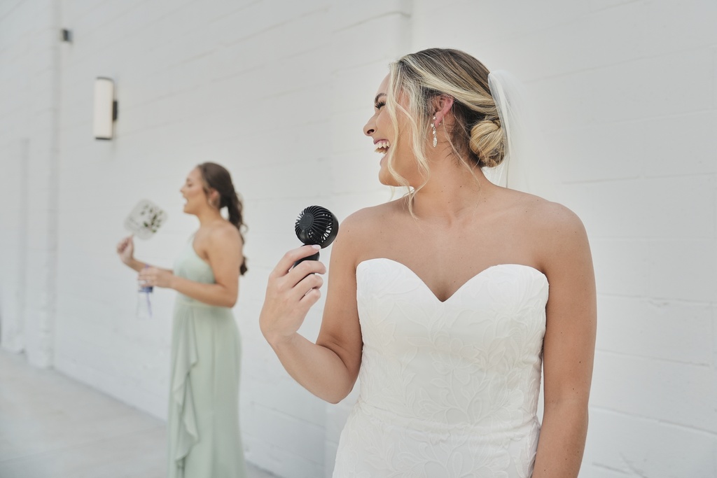 Kayla McDonald, right, uses a small electric fan to keep cool while taking bridal portraits with her sister, Jessica McDonald, left, before her wedding Saturday, Aug. 23, 2025, in Newtown, Ohio. (AP Photo/Joshua A. Bickel)