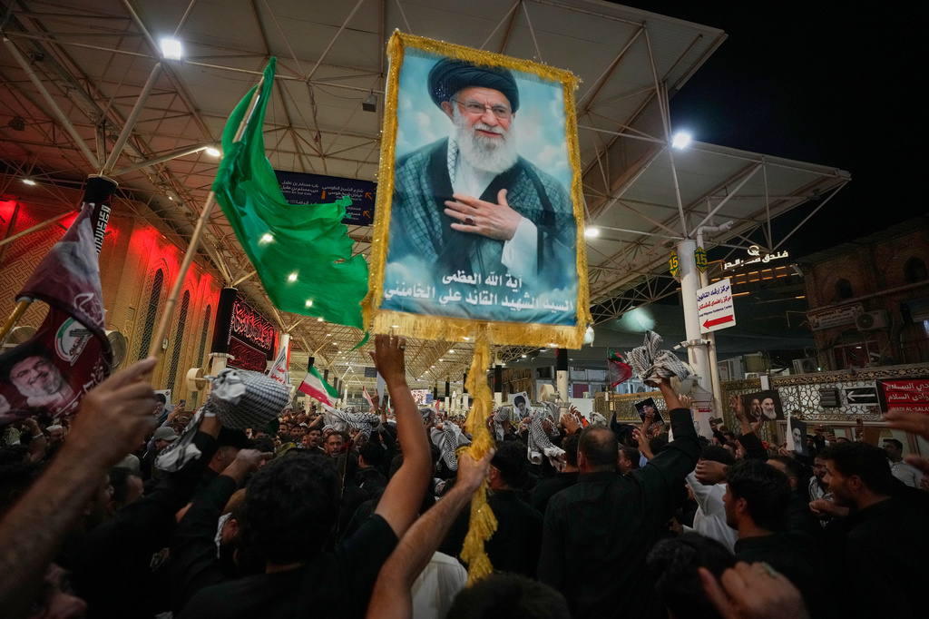 Mourners wave Shiite religious flags and carry a portrait of the late Iranian Supreme Leader Ayatollah Ali Khamenei outside the Imam Ali Shrine on the eve of funeral ceremonies in Najaf, Iraq, Tuesday, July 7, 2026. (AP Photo/Hadi Mizban)
