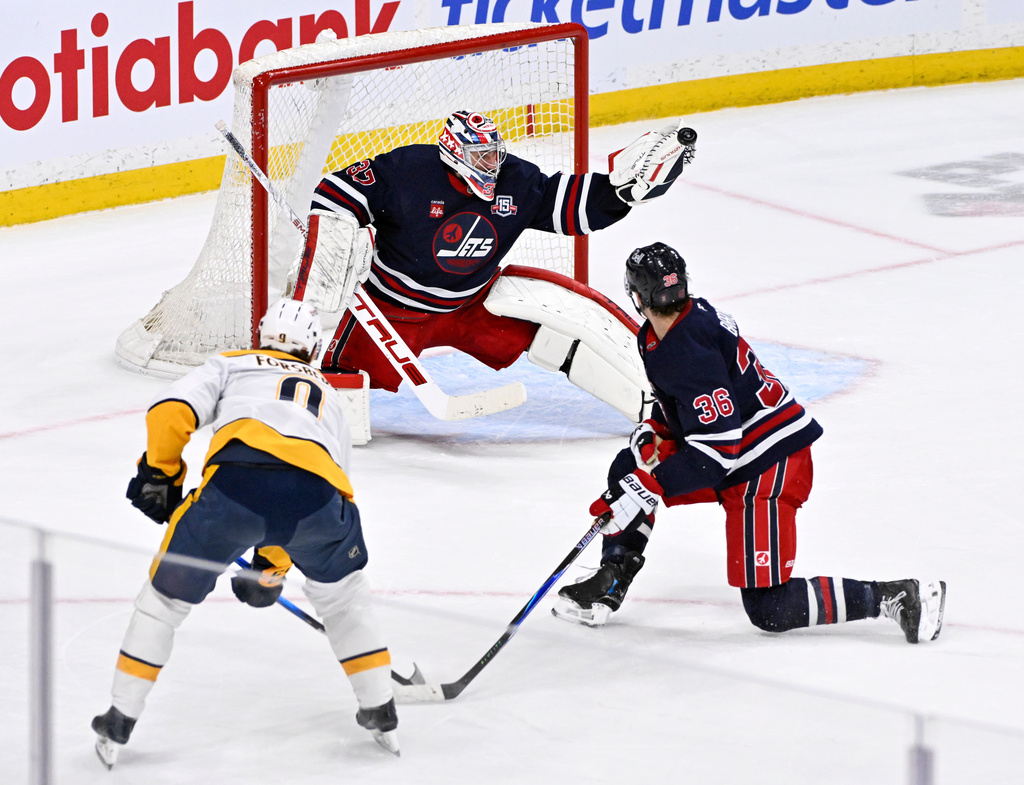 Winnipeg Jets goaltender Connor Hellebuyck (37) makes a save on Nashville Predators' Filip Forsberg (9) as Morgan Barron (36) defends during the overtime period of their NHL hockey game in Winnipeg, Tuesday March 17, 2026. (Fred Greenslade/The Canadian Press via AP)
