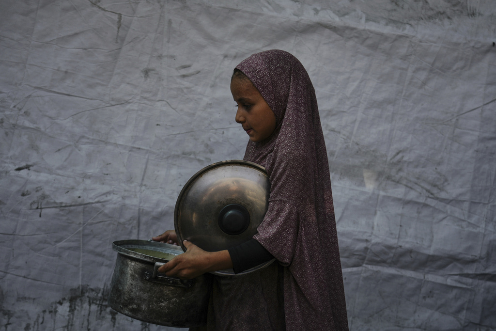 A Palestinian child carries a pot of donated food from a community kitchen in Deir al-Balah, southern Gaza Strip, Saturday, Sept. 6, 2025. (AP Photo/Jehad Alshrafi)