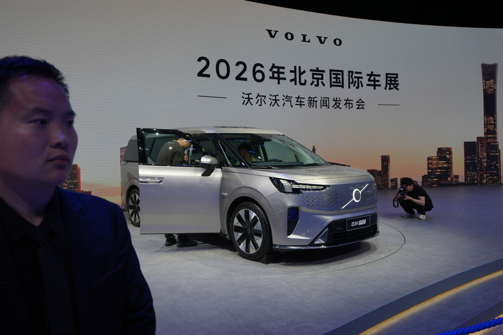 A security stands watch as visitors look at the Volvo EM90 model showcased at the Auto China 2026, in Beijing, Friday, April 24, 2026. (AP Photo/Andy Wong)