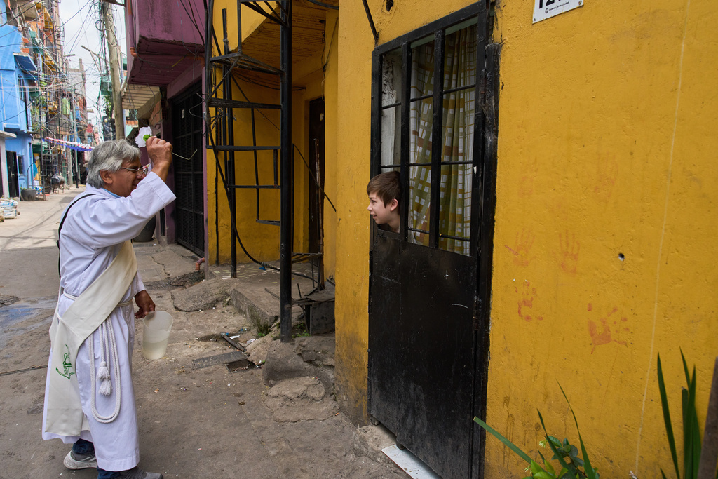 FILE - Catholic deacon Mario Rene Garcia sprinkles holy water with a blessing for Martial Martinez as he peeks out from a window during a procession celebrating the feast day of Paraguay's patroness, Our Lady of Caacupe, popularly known as the Blue Virgin, in Buenos Aires, Argentina, Dec. 8, 2025. (AP Photo/Rodrigo Abd, File)