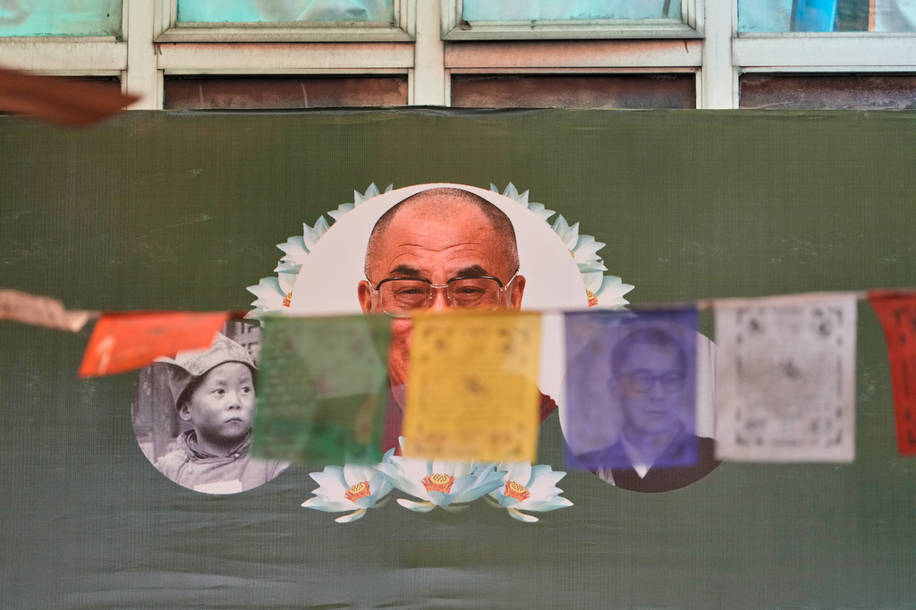 Prayer flags flutter in front of a banner depicting Tibetan spiritual leader the Dalai Lama in childhood, youth and the present day during celebrations marking his birthday, at a Tibetan school in New Delhi, India, Monday, July 6, 2026. (AP Photo/Manish Swarup)