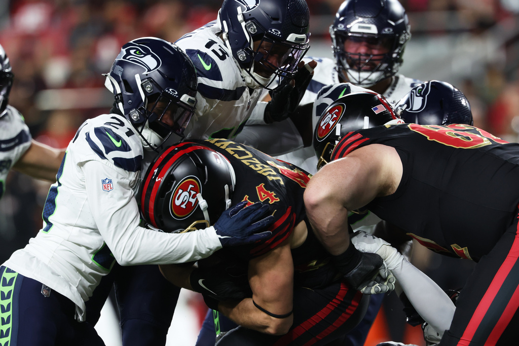 San Francisco 49ers fullback Kyle Juszczyk, bottom middle, is stopped by Seattle Seahawks cornerback Devon Witherspoon (21) and linebacker Ernest Jones IV (13) during the first half of an NFL football game in Santa Clara, Calif., Saturday, Jan. 3, 2026. (AP Photo/Jed Jacobsohn)