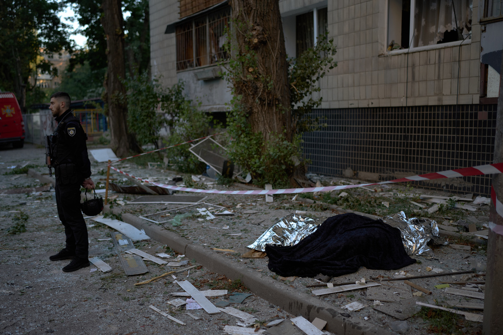 A policeman stands next to the bodies of two people killed during an overnight Russian attack in Kyiv, Ukraine, Thursday, Aug. 20, 2026. (AP Photo/Francisco Seco)