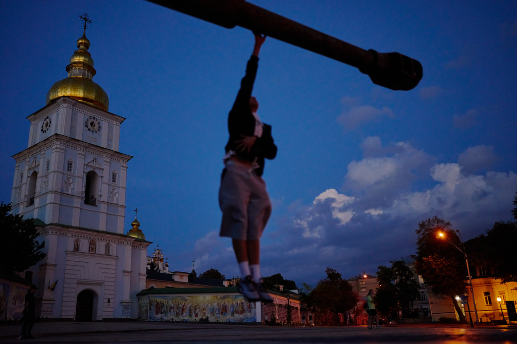 A youth jumps to touch the cannon of a captured Russian tank as he walks past it on display in Sofiyivska square, next to Saint Michael Cathedral in Kyiv, Ukraine, Sunday, Aug. 30, 2026. (AP Photo/Francisco Seco)