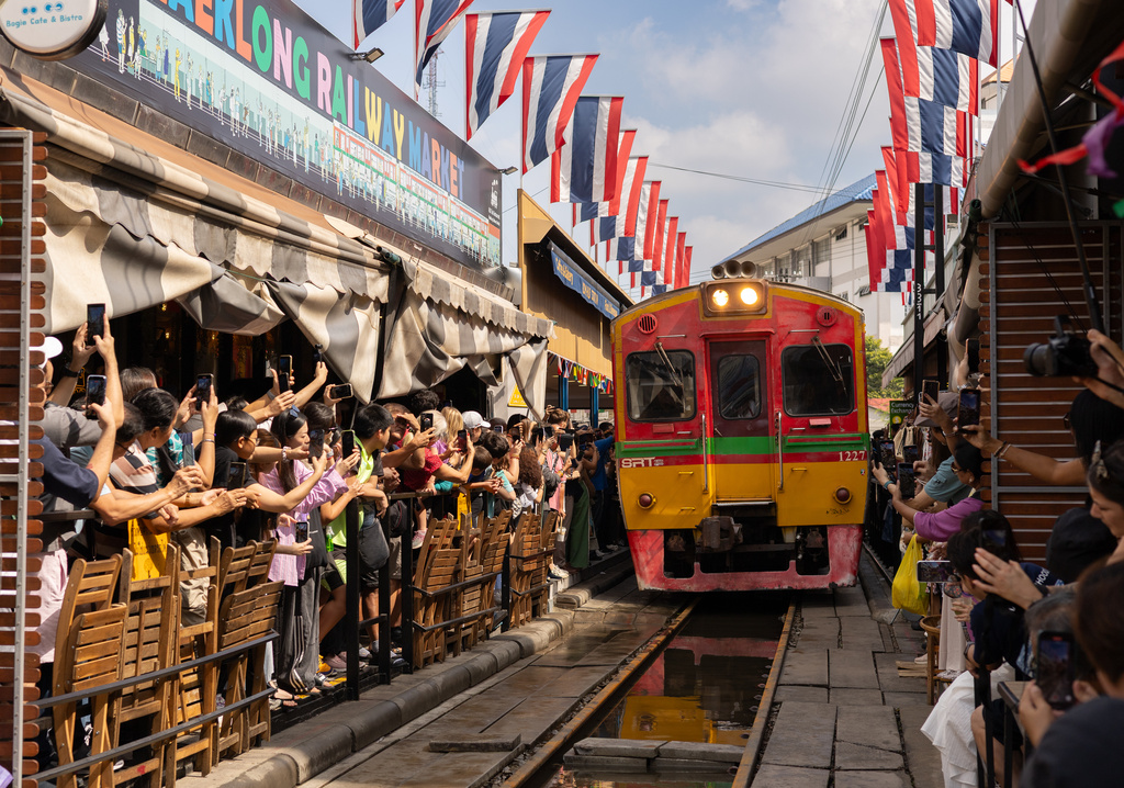A crowd of tourists take pictures of a passing train at the Mae Klong Railway Market near Bangkok, Thailand on Dec. 6, 2025. (AP Photo/Anton L. Delgado)