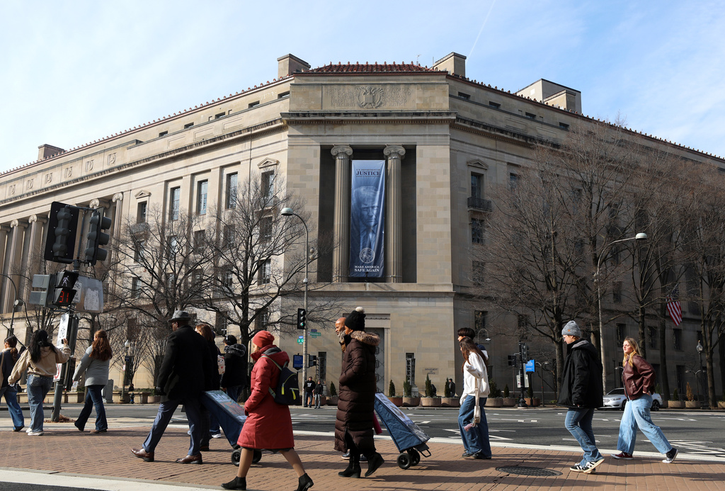 FILE - Tourists walk past a banner with President Donald Trump hanging on the Department of Justice, Feb. 27, 2026, in Washington. (AP Photo/Rahmat Gul, File)