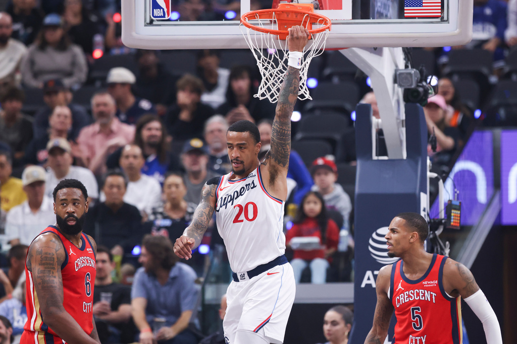 Los Angeles Clippers forward John Collins (20) hangs on the basket after dunking as New Orleans Pelicans guard Dejounte Murray (5) watches and center DeAndre Jordan (6) looks on during the first half of an NBA basketball game, Sunday, March 1, 2026, in Inglewood, Calif. (AP Photo/Jessie Alcheh)