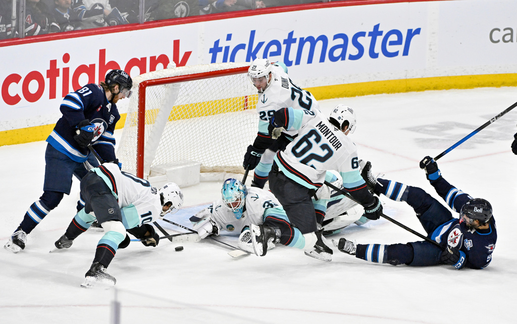 Seattle Kraken goaltender Joey Daccord, third from left, scrambles to make a save against Winnipeg Jets' Kyle Connor (81) as Kraken's Matty Beniers (10), Vince Dunn (29) and Brandon Montour (62) defend during third-period NHL hockey game action in Winnipeg, Manitoba, Monday, April 6, 2026. (Fred Greenslade/The Canadian Press via AP)