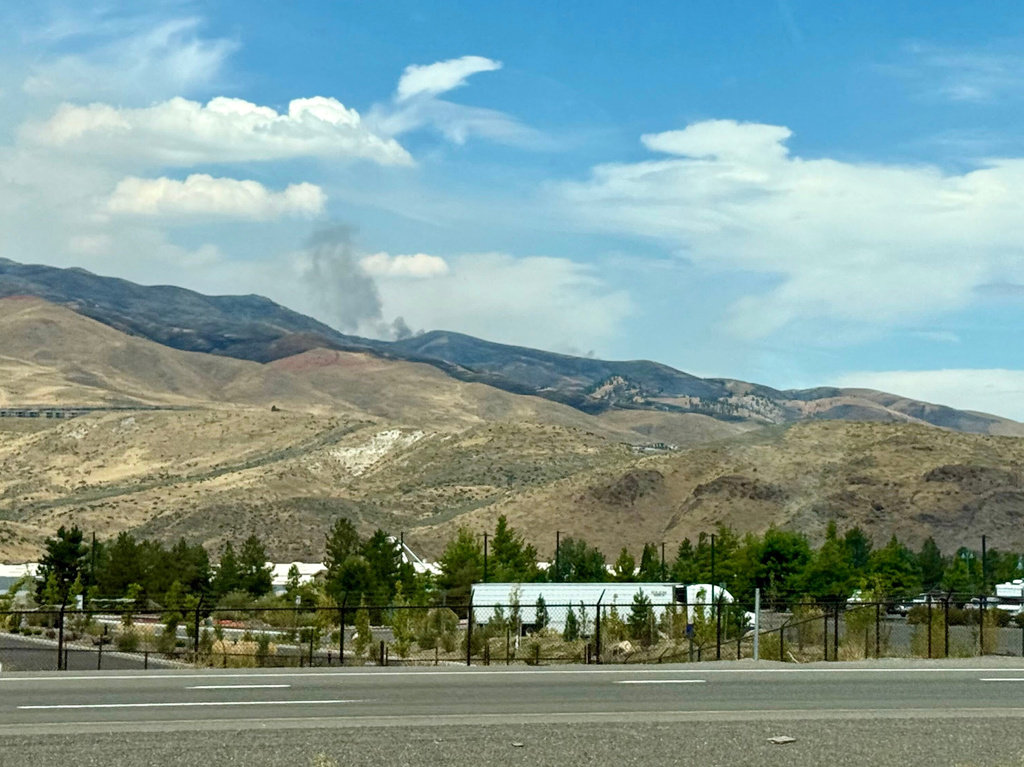 Smoke billows in the distance as a wildfire in Reno, Nev., destroyed homes and caused thousands to evacuate their homes, Sunday, August 23, 2026. (AP Photo/Haven Daley)