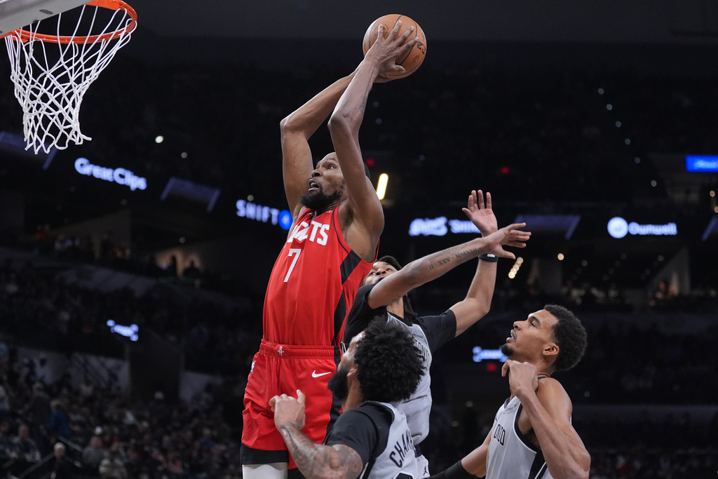 Houston Rockets forward Kevin Durant (7) drives to the basket past San Antonio Spurs forward Julian Champagnie (30) and San Antonio Spurs forward Victor Wembanyama, right, during the second half of an NBA Cup basketball game in San Antonio, Friday, Nov. 7, 2025. (AP Photo/Eric Gay)