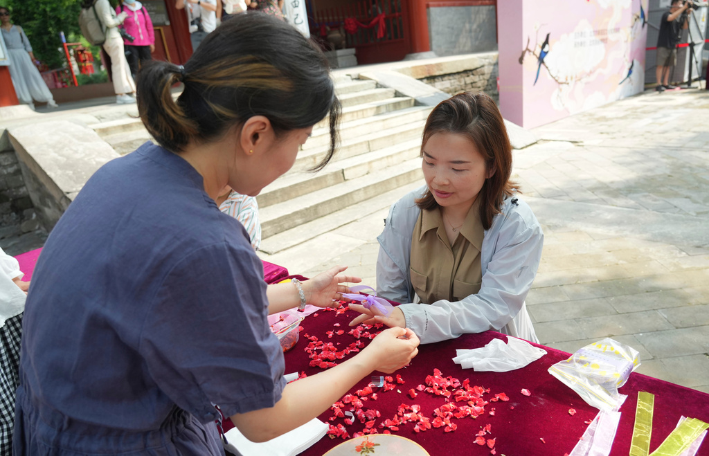 A woman gets her nail dyed with garden balsam, a natural pigment traditionally associated with beauty and blessings, during a festival to celebrate Qixi at the Beijing Folk Custom Museum in Beijing, Wednesday, Aug. 19, 2026. (AP Photo/Achmad Ibrahim)