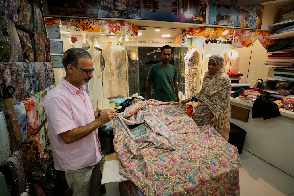 People examine embroidered fabric at a textile shop in a traditional bazaar in Bandar Abbas, Iran, Sunday, Sept. 6, 2026. (AP Photo/Vahid Salemi)