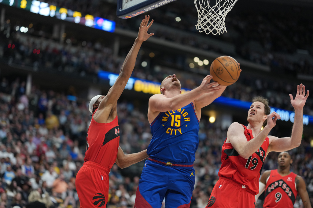 Denver Nuggets center Nikola Jokic drives to the basket between Toronto Raptors forward Brandon Ingram, left, and center Jakob Poeltl, right, in the first half of an NBA basketball game Friday, March 20, 2026, in Denver. (AP Photo/David Zalubowski)