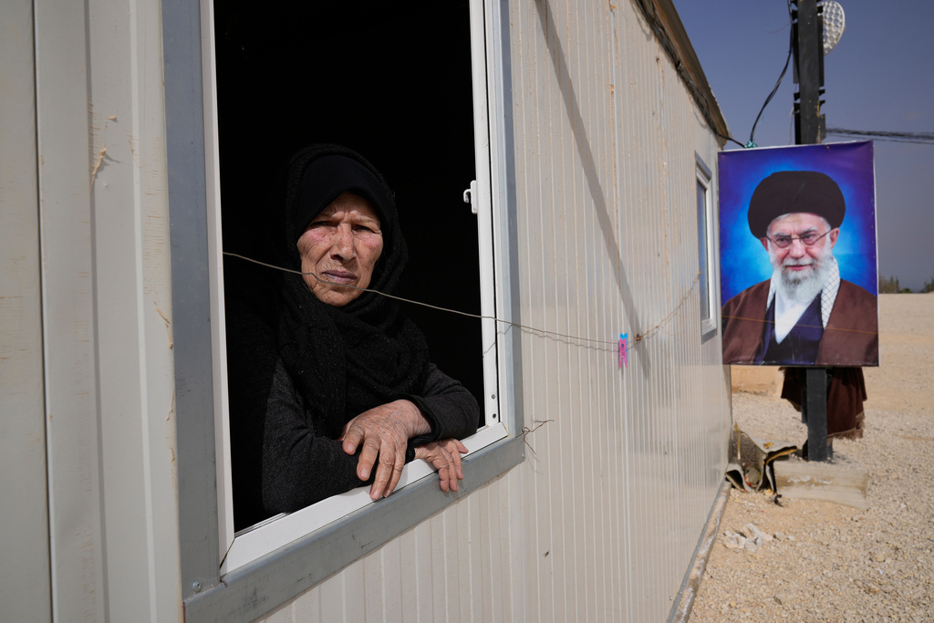 Souria al-Hassan, 75, a Syrian Shiite woman, looks out from the window of her housing unit next to a portrait of Iranian Supreme Leader Ayatollah Ali Khamenei at the Imam Ali Housing Compound, where hundreds of mostly Lebanese and Syrian Shiite Muslims displaced from Syria reside, in Hermel, northeast Lebanon, Friday, Jan. 30, 2026. (AP Photo/Hussein Malla)