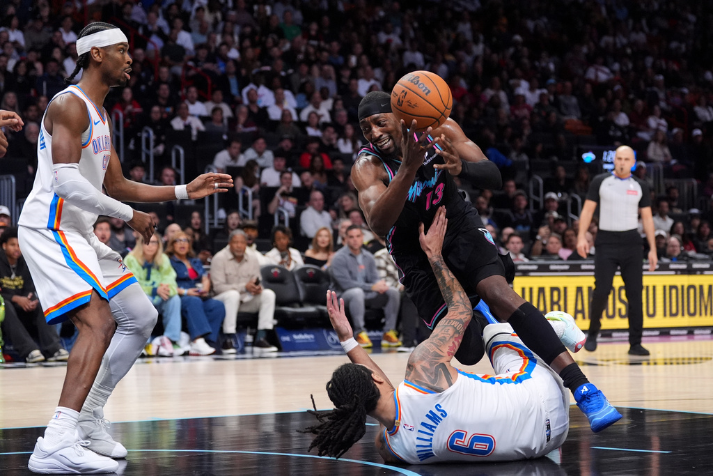 Miami Heat center Bam Adebayo (13) falls as he is fouled by Oklahoma City Thunder forward Jaylin Williams (6) as guard Shai Gilgeous-Alexander looks on during the first half of an NBA basketball game, Saturday, Jan. 17, 2026, in Miami. (AP Photo/Rebecca Blackwell)