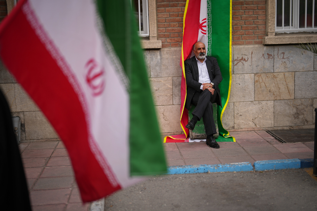 A man sits beside an Iranian flag banner during a government-sponsored protest attended by medical workers against the U.S.-Israeli military campaign outside Imam Khomeini Hospital in Tehran, Iran, Monday, April 6, 2026. (AP Photo/Francisco Seco)