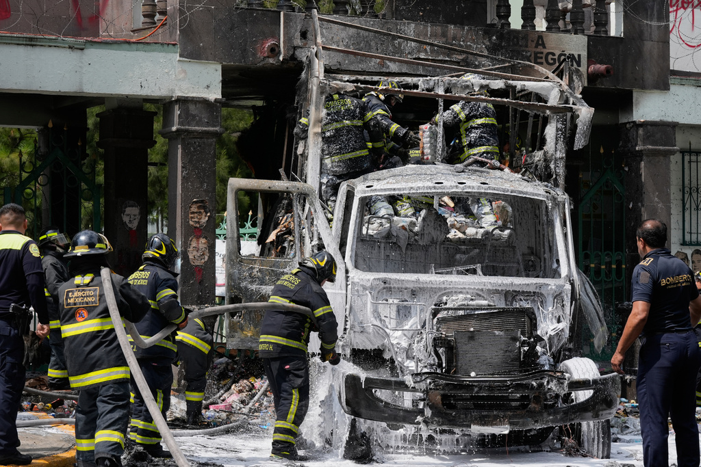 Firefighters extinguish a garbage truck that demonstrators set on fire during a protest marking the 11th anniversary of the disappearance of 43 students from an Ayotzinapa rural teacher's college, outside the entrance of Campo Militar, in Mexico City, Thursday, Sept. 25, 2025. (AP Photo/Fernando Llano)