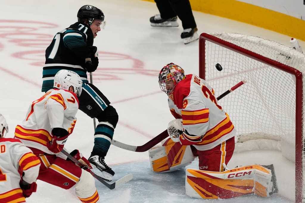 San Jose Sharks center Macklin Celebrini (71) scores a goal past Calgary Flames goaltender Dustin Wolf, right, during the third period of an NHL hockey game in San Jose, Calif., Tuesday, Dec. 16, 2025. (AP Photo/Jeff Chiu)