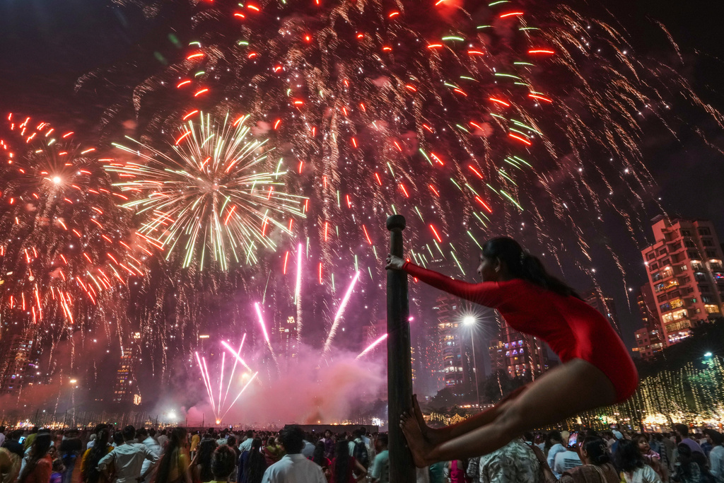 A girl performs on a mallakhamb pole as fireworks light up the sky during the festival of lights Diwali in Mumbai, India, on Monday, Oct. 20, 2025. (AP Photo/Rafiq Maqbool)