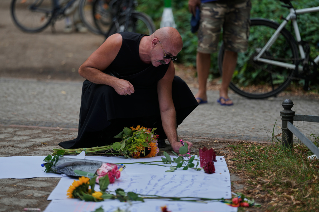 A man writes a message on a board at the memorial site commemorating the victims near the scene where a car rammed into a crowd near the Pride March in Berlin, Germany, Sunday, July 26, 2026. (AP Photo/Markus Schreiber)