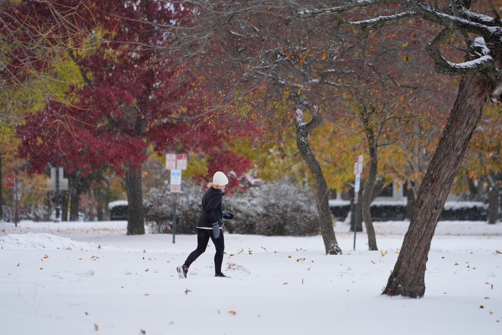 A person jogs as snow covers the ground with fall colors on the trees in Evanston, Ill., a suburb of Chicago, Monday, Nov. 10, 2025. (AP Photo/Kiichiro Sato)