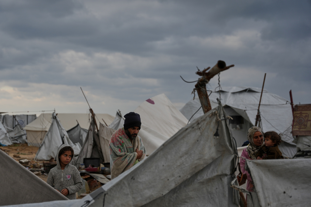 Wrapped in a blanket, Raafat Alwan, 32, stands outside his tent with his family in a makeshift camp for displaced Palestinians set up on the beach during a cold morning in Gaza City, Tuesday, Dec. 16, 2025. (AP Photo/Abdel Kareem Hana)