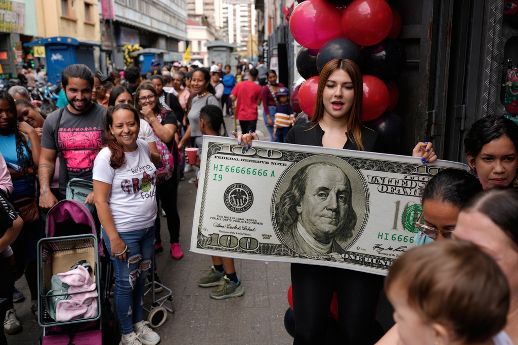 A model holds a Ben Franklin–themed banknote rug that will be raffled off as shoppers wait in line for Black Friday bargains in Caracas, Venezuela, Friday, Nov. 28, 2025. (AP Photo/Ariana Cubillos)