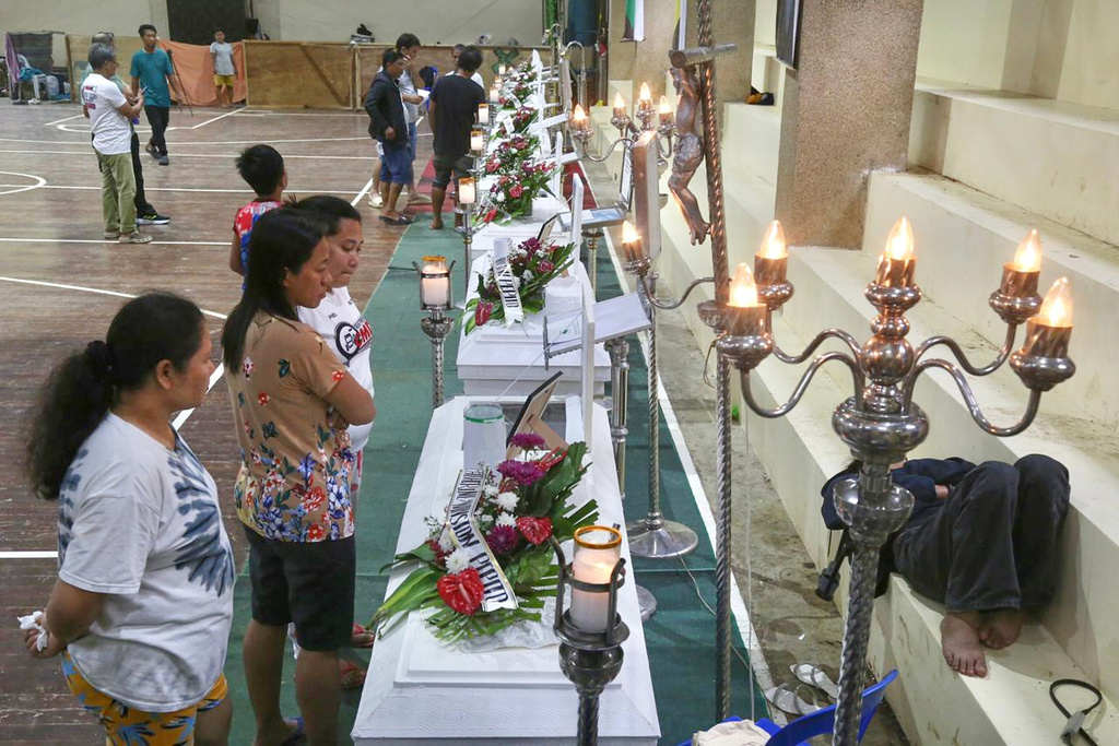 Relatives and friends stand near coffins in Bacayan, Cebu province, Philippines on Friday Nov. 7, 2025 after Typhoon Kalmaegi devastated the province and claimed lives. (AP Photo/Jacqueline Hernandez)