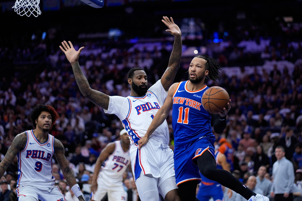 New York Knicks' Jalen Brunson, right, passes against Philadelphia 76ers' Andre Drummond during the first half of Game 3 in a second-round NBA basketball playoff series Friday, May 8, 2026, in Philadelphia. (AP Photo/Matt Slocum)