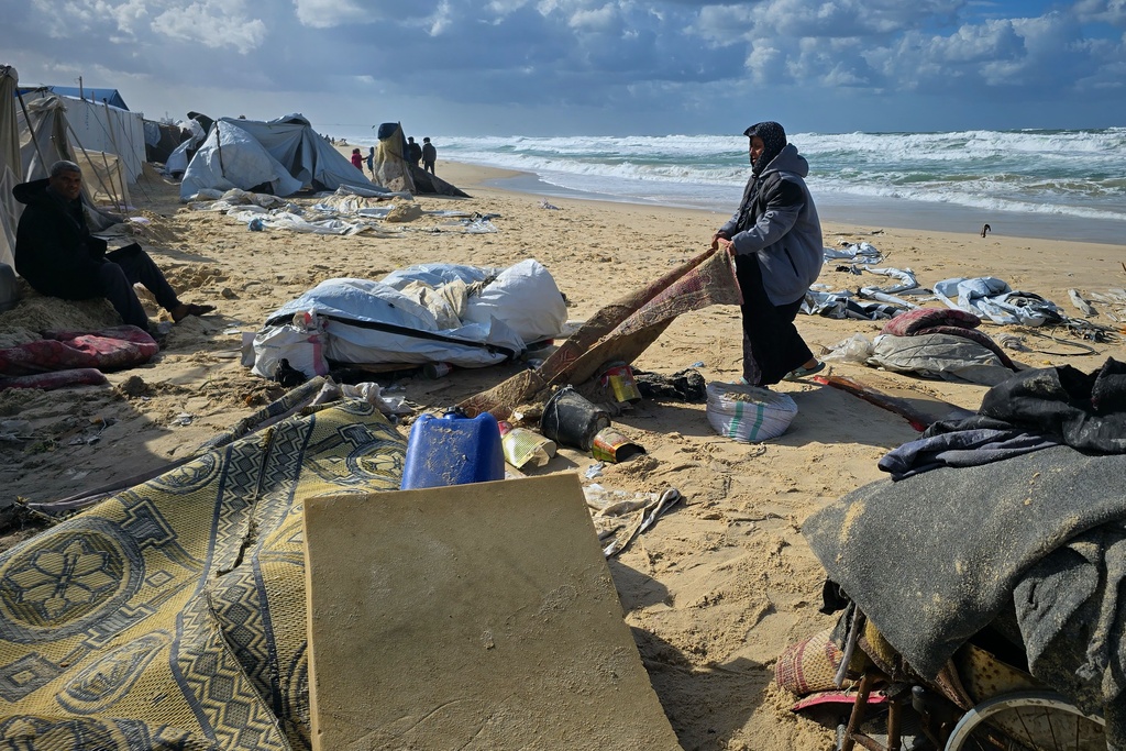 A woman tries to recover a carpet after overnight rainfall flooded a beachside tent camp in Khan Younis, in the southern Gaza Strip, Sunday, Dec. 28, 2025. (AP Photo/Mohammad Jahjouh)