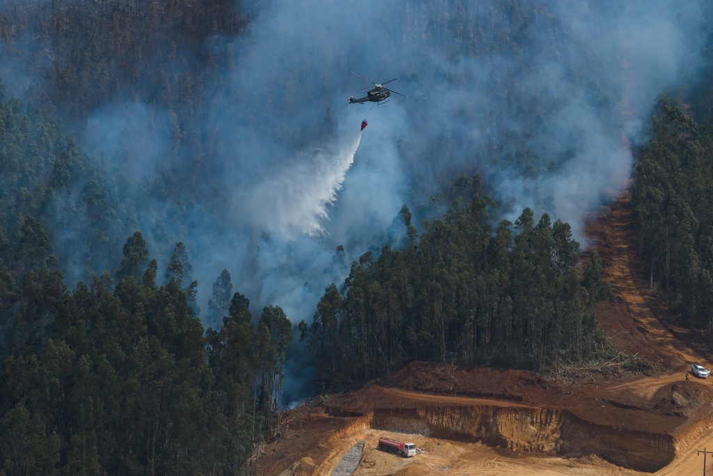 A helicopter drops water to battle wildfires near Concepcion, Chile, Monday, Jan. 19, 2026. (AP Photo/Javier Torres)