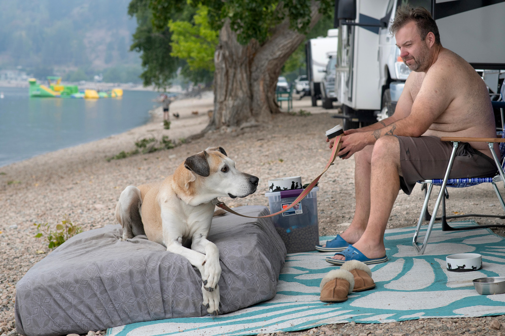 Matt Prouxl sits with his dog, Baily, by his RV trailer, along Beach Avenue in Peachland, British Columbia, Canada, on Saturday, Aug. 8, 2026. Matt, his wife and 18-year-old daughter, along with two other dogs, were evacuated from their home on Princeton Avenue the night before. (Gary Nylander/The Canadian Press via AP)