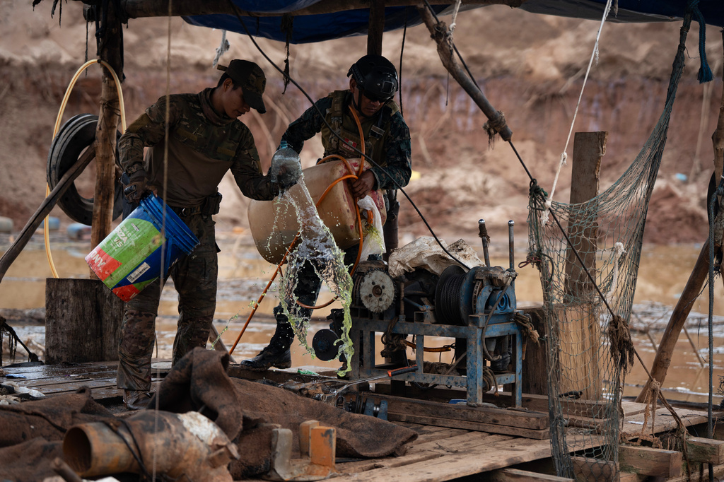 Peruvian Navy soldiers pour gasoline onto a dredge during an operation to combat illegal mining in the Tambopata National Reserve in Puerto Maldonado, Peru, Tuesday, Aug. 11, 2026. (AP Photo/Guadalupe Pardo)
