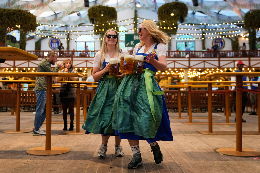 Waitresses celebrate in a beer tent after the re-opening of the Oktoberfest watched by police officers that was closed since the morning after a bomb threatening in Munich, Germany, Wednesday, Oct.1, 2025. (AP Photo/Matthias Schrader)