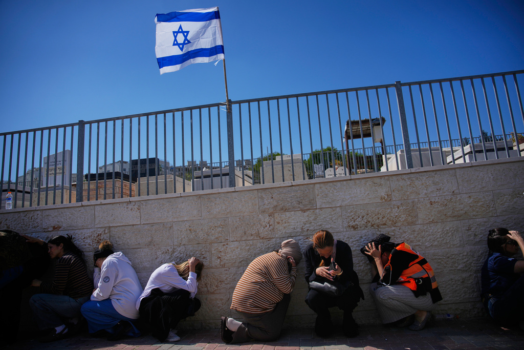 Mourners take cover while air-raid sirens warn of incoming missiles launched by Iran toward Israel during the funeral of Sarah Elimelech and her daughter Ronit who were killed in an Iranian missile attack, in Beit Shemesh, Israel, Monday, March 2, 2026. (AP Photo/Ohad Zwigenberg)