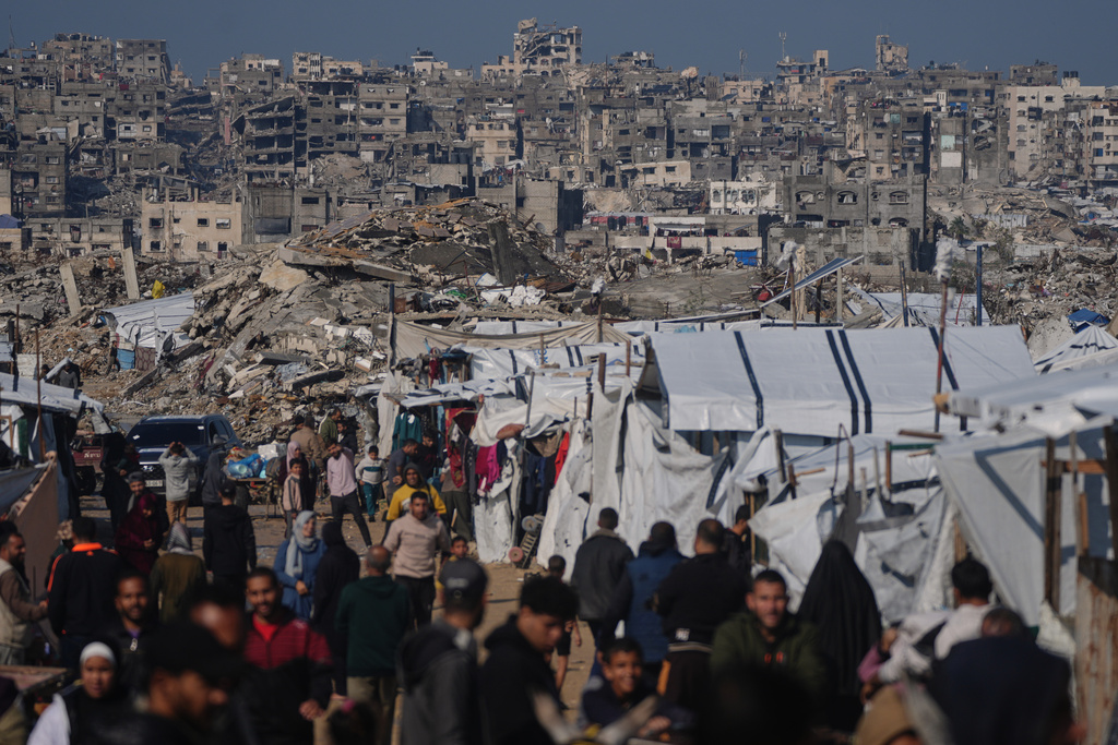 FILE - Palestinians walk along a street past a tent camp, backdropped by buildings destroyed during Israeli air and ground operations in Gaza City, Wednesday, Dec. 17, 2025. (AP Photo/Jehad Alshrafi, File)